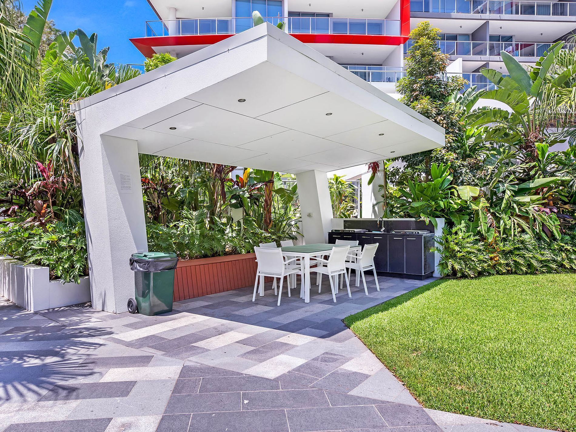An outdoor patio with a covered seating area, a grill, and lush tropical plants.