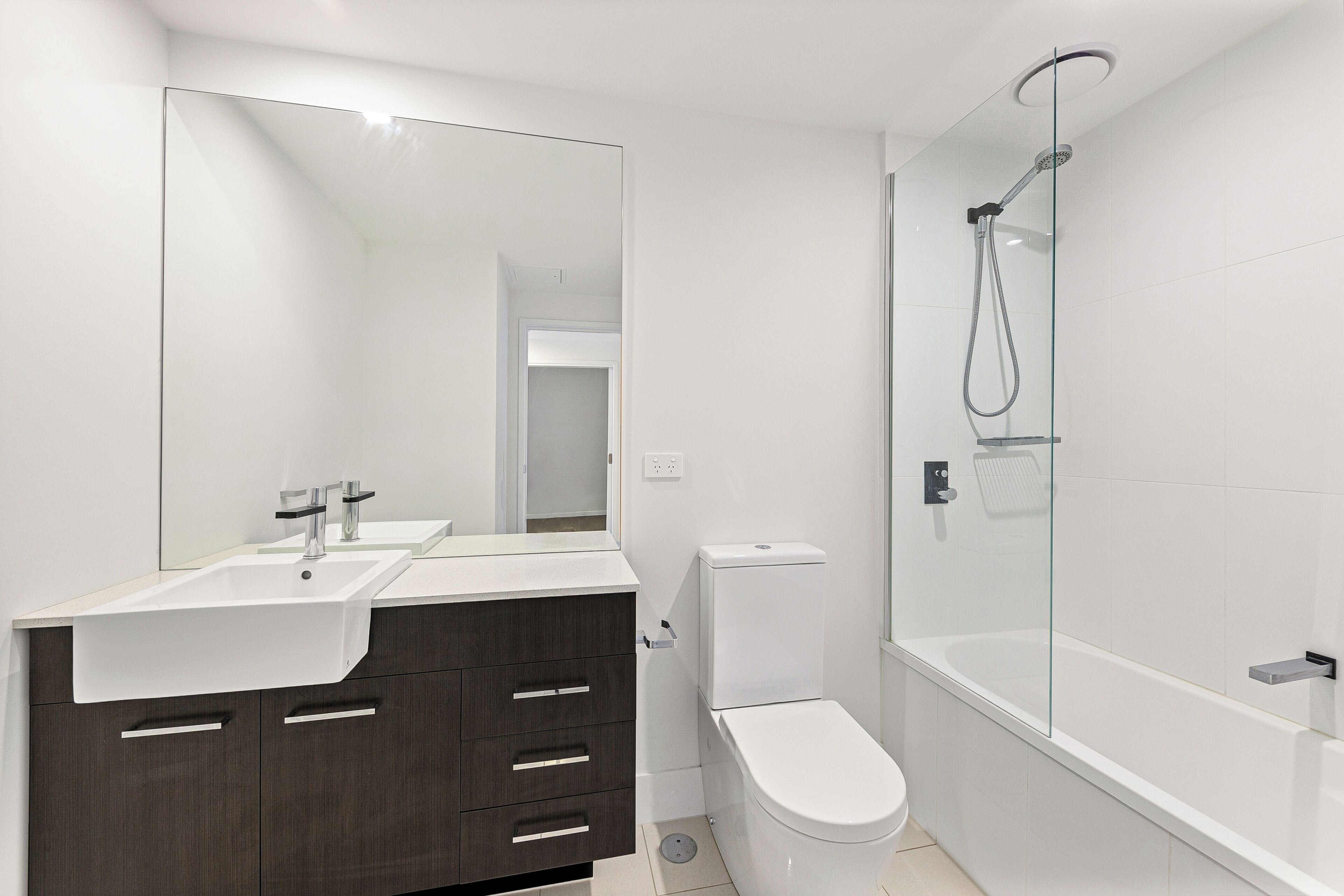 A modern bathroom with a white sink, dark wooden vanity, a toilet, and a glass-enclosed shower area.