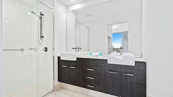 A modern bathroom with a glass shower enclosure, two sinks, dark wood cabinets, and a large mirror.