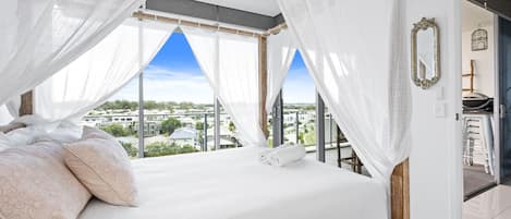 A bedroom with a bed, white bedding, and a view of a residential area.