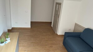 A room with a wooden floor, a blue sofa, a small table with potted plants, and a door with a sign. - A1 SOLE - APARTMENT WITH 6 BEDS (Balestrate)