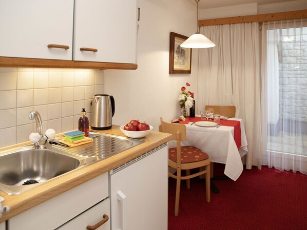 Une cuisine compacte équipée d’un évier, d’une bouilloire et d’un coin repas avec une table dressée pour deux personnes.