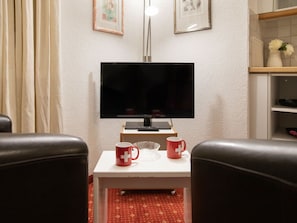 Una sala de estar con un televisor de pantalla plana, dos tazas rojas, una mesita y un tapete con estampado rojo.
