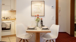 Un coin repas avec une table dressée pour deux personnes, une cuisine en arrière-plan et une œuvre d’art encadrée accrochée au mur.