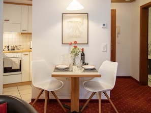 Uma área de refeições com uma mesa posta para dois, uma cozinha ao fundo e uma obra de arte emoldurada na parede.