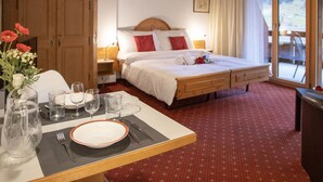 Une chambre d’hôtel avec un lit, une table à manger dressée avec des assiettes, des verres et des couverts, une armoire en bois et une vue par la fenêtre.