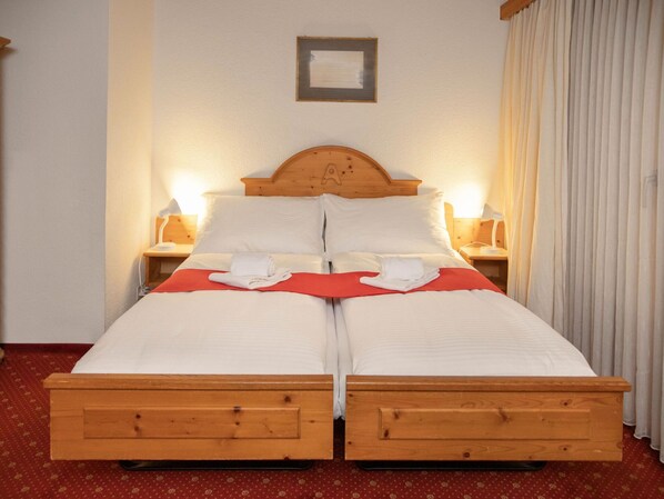 Uma cama de casal com cabeceira de madeira, roupa de cama branca, duas mesas de cabeceira com luminárias e um cobertor vermelho.