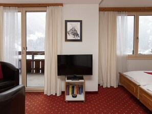 Une chambre avec un lit, un téléviseur posé sur un meuble, une bibliothèque et une vue sur un paysage enneigé par les fenêtres.