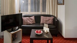 A living room with a black leather sofa, a flat-screen TV on a stand, a small table with a bowl of apples, and a painting on the wall.