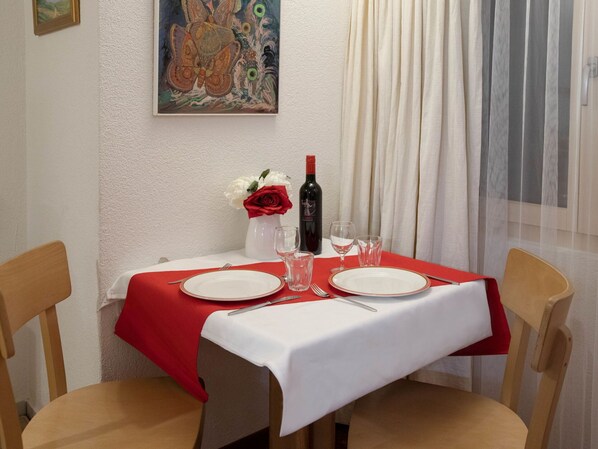 Una mesa de comedor dispuesta con platos, cubiertos y una botella de vino, con un cuadro y un jarrón de flores en la pared.