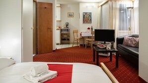 A hotel room with a bed, a TV, a sofa, a desk, and a kitchenette.