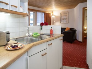 Une cuisine équipée d’un évier, d’un grille-pain et d’une assiette avec des toasts. Il y a une fenêtre avec des rideaux et un tableau encadré accroché au mur.