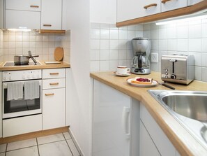 Uma cozinha moderna com armários brancos, uma pia de aço inoxidável, uma cafeteira, uma torradeira e uma chaleira.