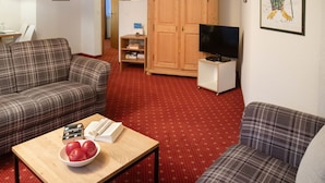 A living room with two sofas, a coffee table with books and apples, a television on a stand, a wooden wardrobe, and a framed picture on the wall.