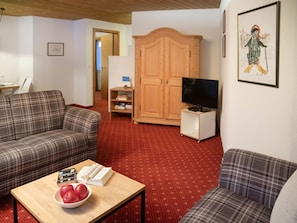 Un salón con dos sofás, una mesa de centro con libros y manzanas, un televisor sobre un mueble bajo, un armario de madera y un cuadro enmarcado en la pared.