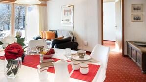 A dining area with a table set for four, a vase with flowers, and a view of the living room.