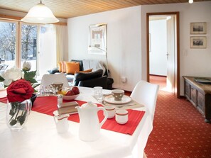 A dining area with a table set for four, a vase with flowers, and a view of the living room.