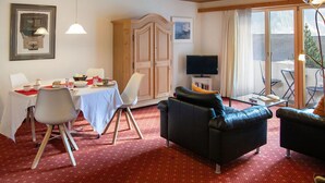 A dining area with a table set for two, a sofa, and a television in a room with wooden ceilings and large windows.