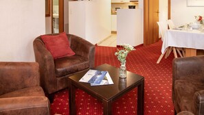 Una sala de estar amoblada con sofá, sillón y una mesa de centro con una revista. Se observa un rincón de comedor con una mesa dispuesta para dos personas al fondo.