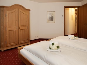 A hotel room with two beds, a wooden wardrobe, a framed picture on the wall, and a red carpeted floor.