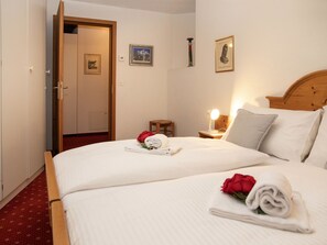 A hotel room with a bed, a nightstand with a lamp, a wooden headboard, a door, and a small stool.