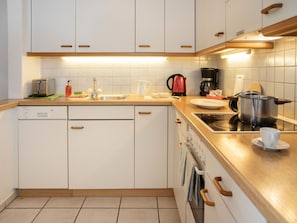 Una cocina moderna con armarios blancos, lavavajillas, estufa y cafetera.