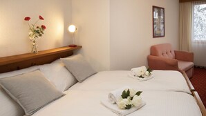 Une chambre d’hôtel avec un lit, des oreillers, une table de chevet ornée d’un vase de fleurs, une chaise et un tableau encadré au mur.
