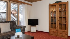 Un salon avec un canapé à carreaux, un téléviseur, un meuble en bois rempli de livres et un tapis rouge.