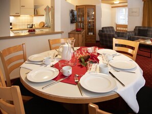 A dining table set for four with white plates, cutlery, and glasses, a pitcher, and a red table runner.