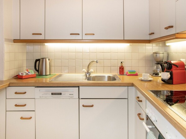 Una cocina con armarios blancos, un lavamanos de acero inoxidable, una cafetera y un lavavajillas.