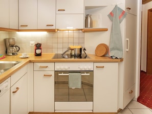 A compact kitchen with white cabinets, a coffee maker, a kettle, and a dish rack.