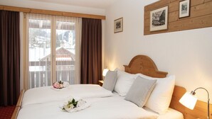 Une chambre d’hôtel avec un lit en bois, une table de chevet avec une lampe, une fenêtre avec des rideaux et des tableaux encadrés au mur.