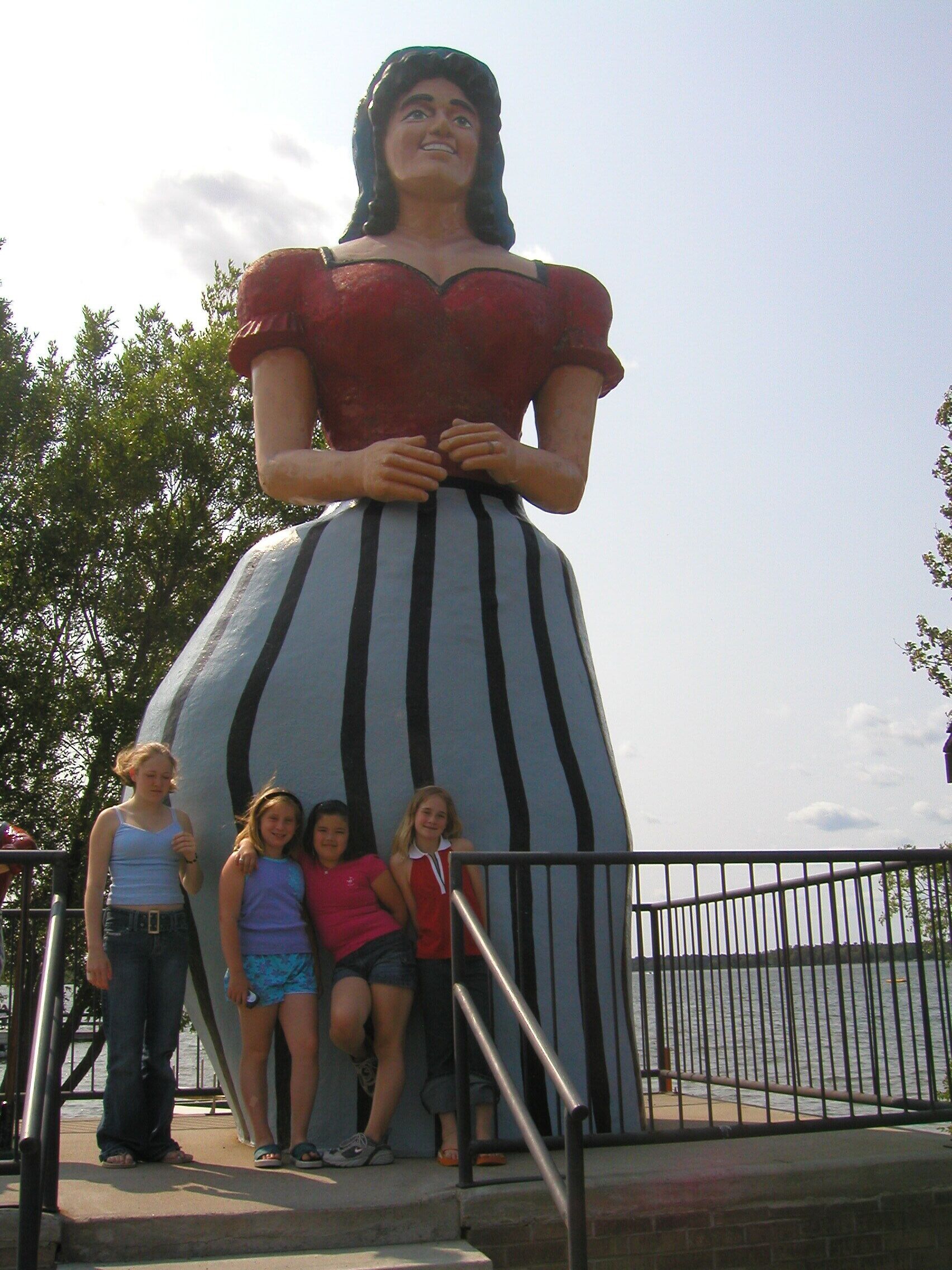 A large statue of a woman in a red dress and striped skirt, with a staircase leading up to it.