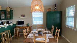 Un coin repas avec une table en bois dressée pour quatre personnes, entourée de chaises en bois. Un luminaire suspendu se trouve au-dessus de la table.