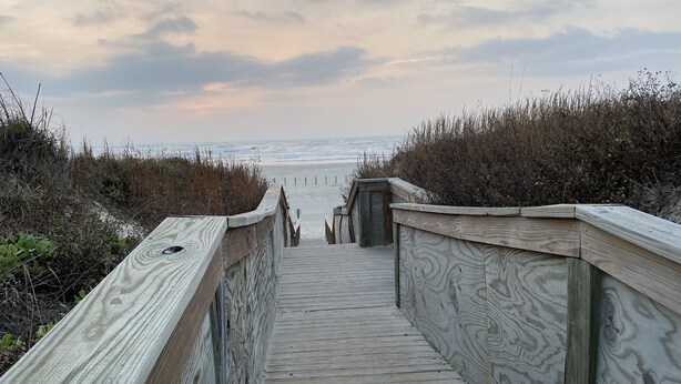 Une promenade en bois menant à une plage, avec un ciel nuageux.