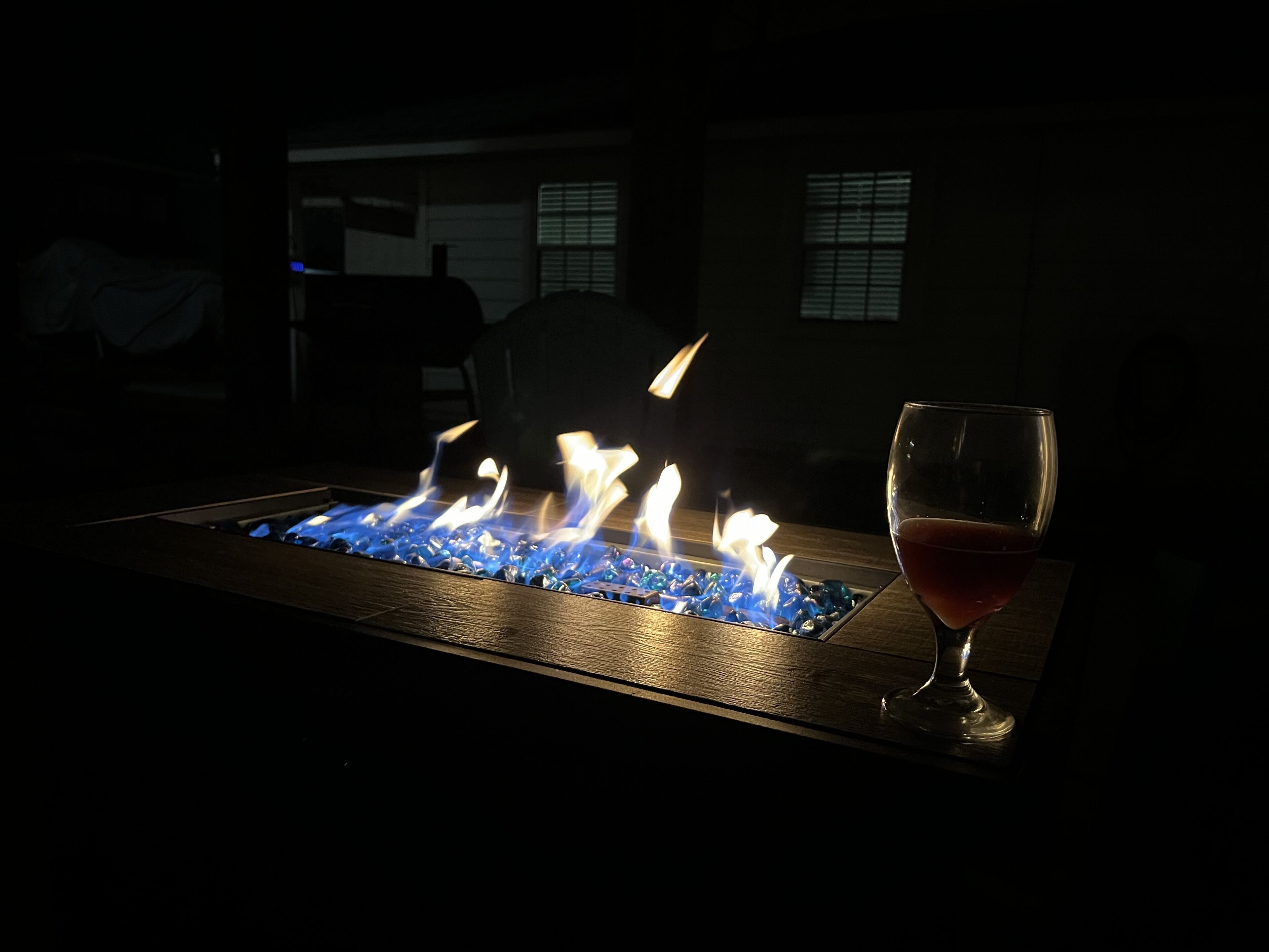 A fire feature with flames and a glass of red wine on a wooden surface.