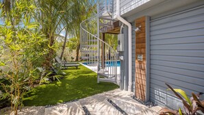 Et moderne hus med en spiraltrappe, der fører op til en træterrasse, en swimmingpool og en velholdt have med forskellige planter.