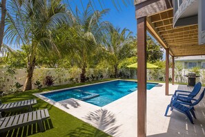 Relax in a serene backyard oasis with a swimming pool surrounded by lush tropical plants and palm trees.