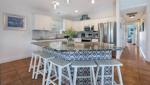 A modern kitchen with white cabinets, stainless steel appliances, and a large island with bar stools. - Meant to Be:1 Block to Beach! North End! Pool & Spa,Loaded Game Room by Anna Maria Life (Anna Maria)