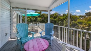 A covered outdoor area with two blue Adirondack chairs, a pink round table, and a white umbrella. - Meant to Be:1 Block to Beach! North End! Pool & Spa,Loaded Game Room by Anna Maria Life (Anna Maria)