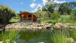 Un chalet rustique doté d’une terrasse en bois et d’un étang devant.