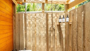 Un espace de douche extérieur en bois, avec un banc en bois, des toilettes et deux bouteilles de shampoing.