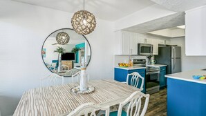 A modern kitchen with white cabinets, a blue island, stainless steel appliances, and a dining area with a striped table and white chairs.