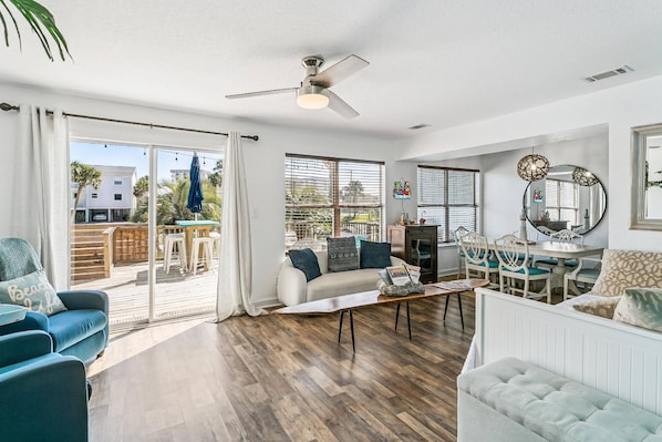 A spacious living area with a sliding glass door to a patio, a ceiling fan, a dining table with chairs, and a sofa with cushions.