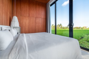 Ein Schlafzimmer mit einem großen Bett, Holzwandverkleidung und Blick auf ein grünes Feld durch ein großes Fenster.