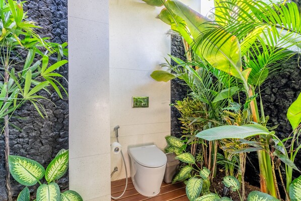 A bathroom with a toilet, a sink, and a shower area surrounded by lush tropical plants.