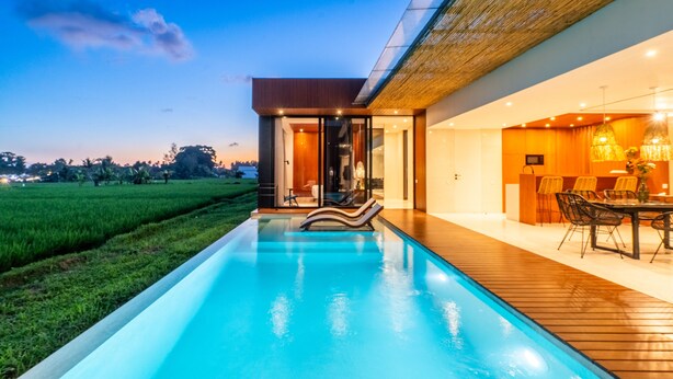 A modern house with a swimming pool, wooden deck, and a dining area with outdoor furniture. - Green Flow Villa 17 (Ubud)