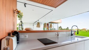 A modern kitchen with a white countertop, a coffee maker, a toaster, and a vase with flowers. - Green Flow Villa 17 (Ubud)