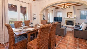 A dining area with wicker chairs, a wooden table set for four, and a fireplace in the background.