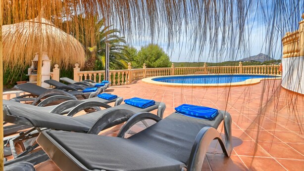 A poolside area with lounge chairs and a thatched umbrella.